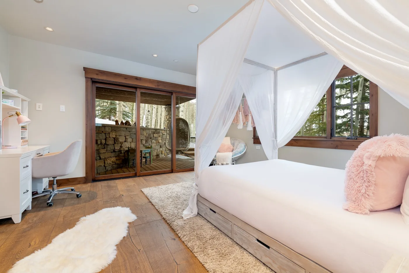 A bright bedroom with a canopied bed, desk, and sliding glass doors.