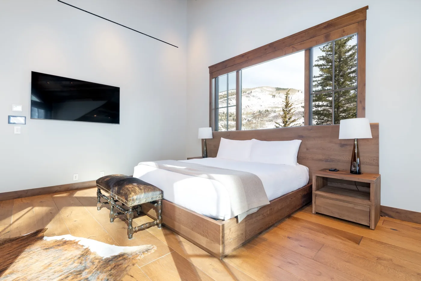 A bedroom with a wooden bed beneath a large window overlooking a snowy landscape.