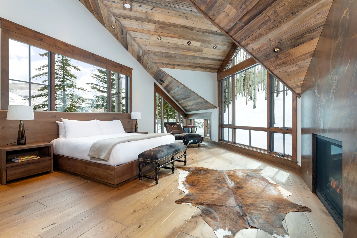 A bedroom with a large bed, wood-paneled ceiling, and tall windows.