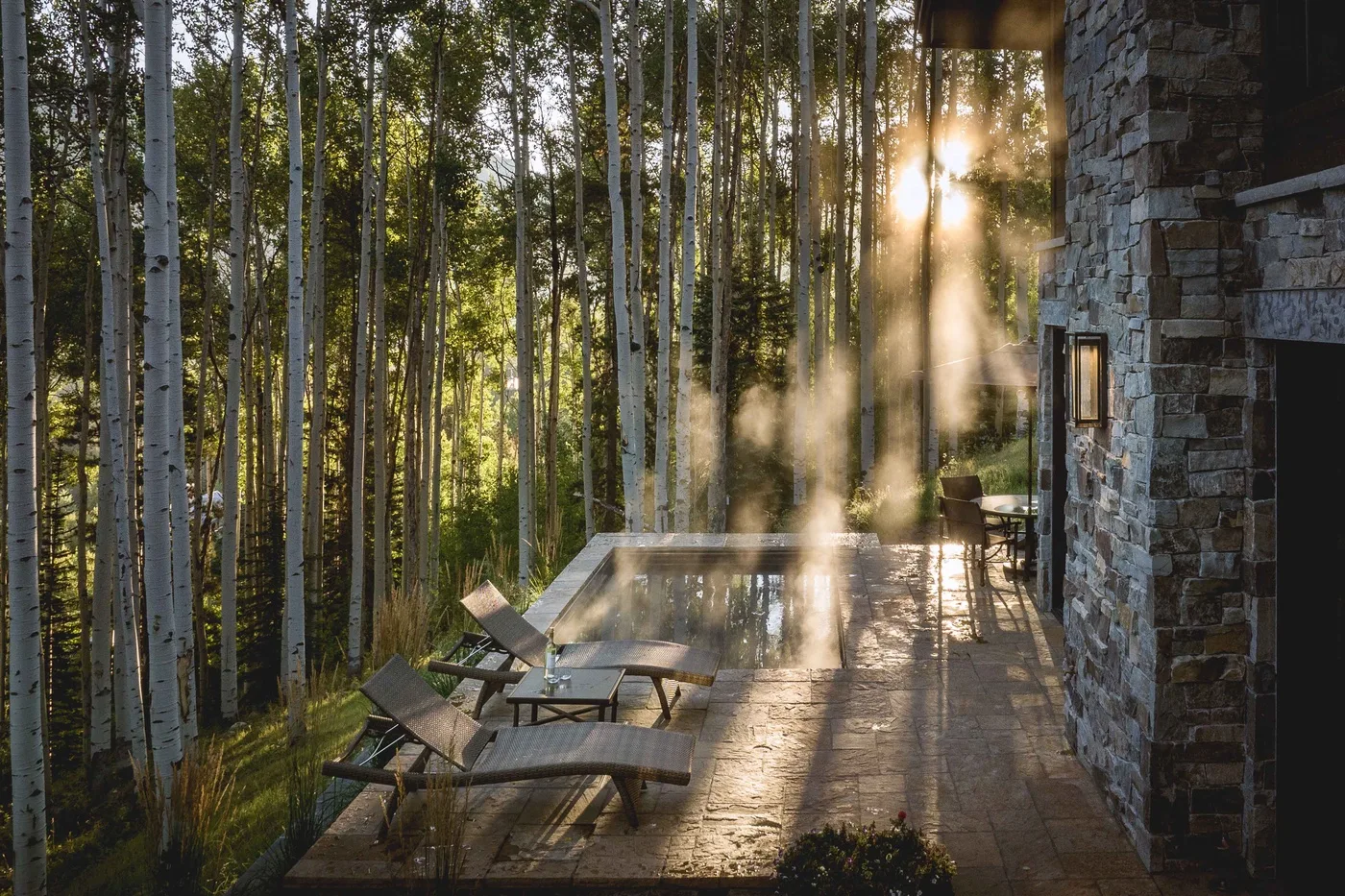 A stone patio beside a steaming outdoor pool, surrounded by trees.