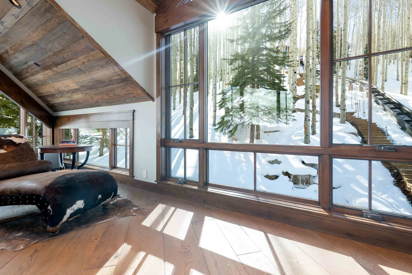 A bright living room with large windows overlooking a snowy, wooded landscape.
