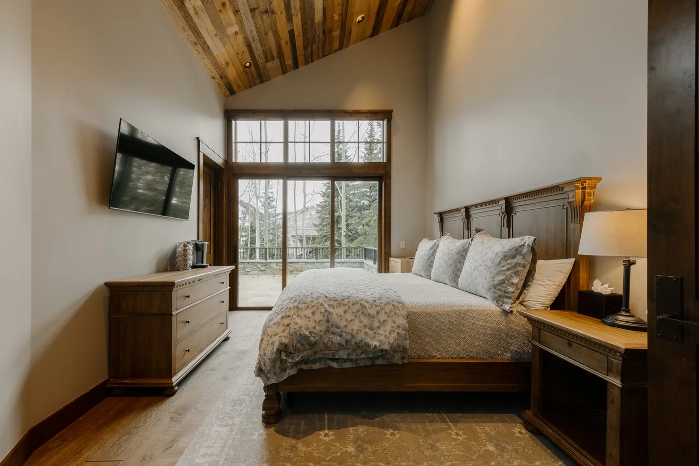 A bedroom with a large bed, wooden furnishings, and tall windows.