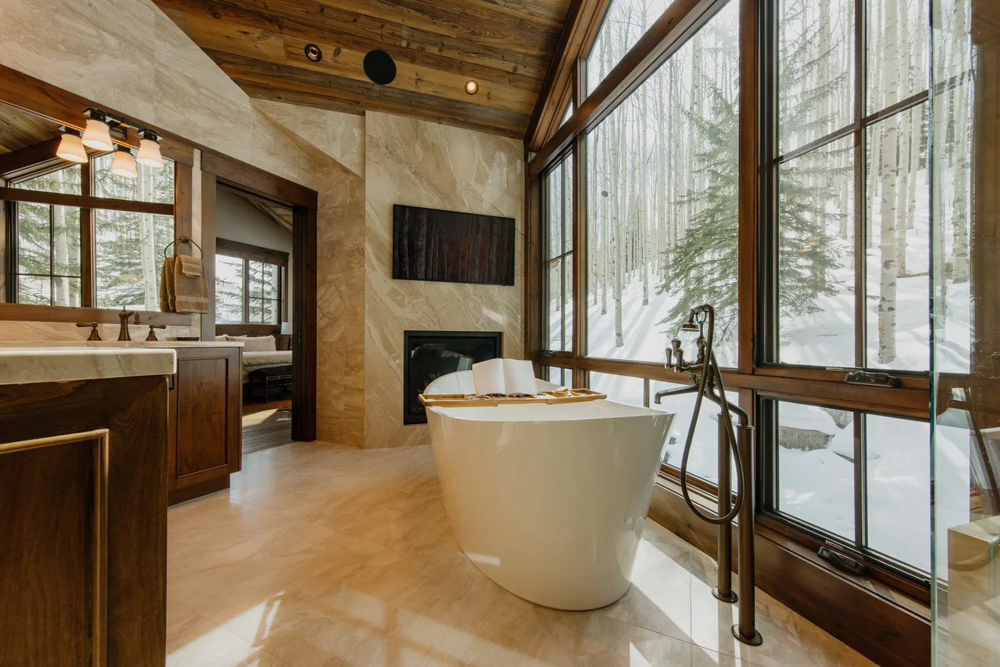 A bright bathroom with a freestanding tub beside large windows overlooking snowy trees.