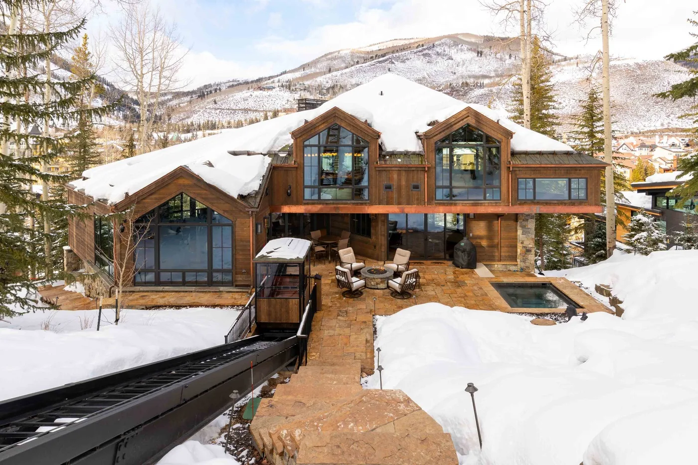 A timber lodge stands in a snowy mountain landscape, with a patio and outdoor pool.