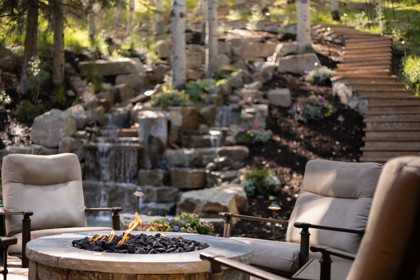 Outdoor seating surrounds a fire pit beside a rocky garden waterfall.