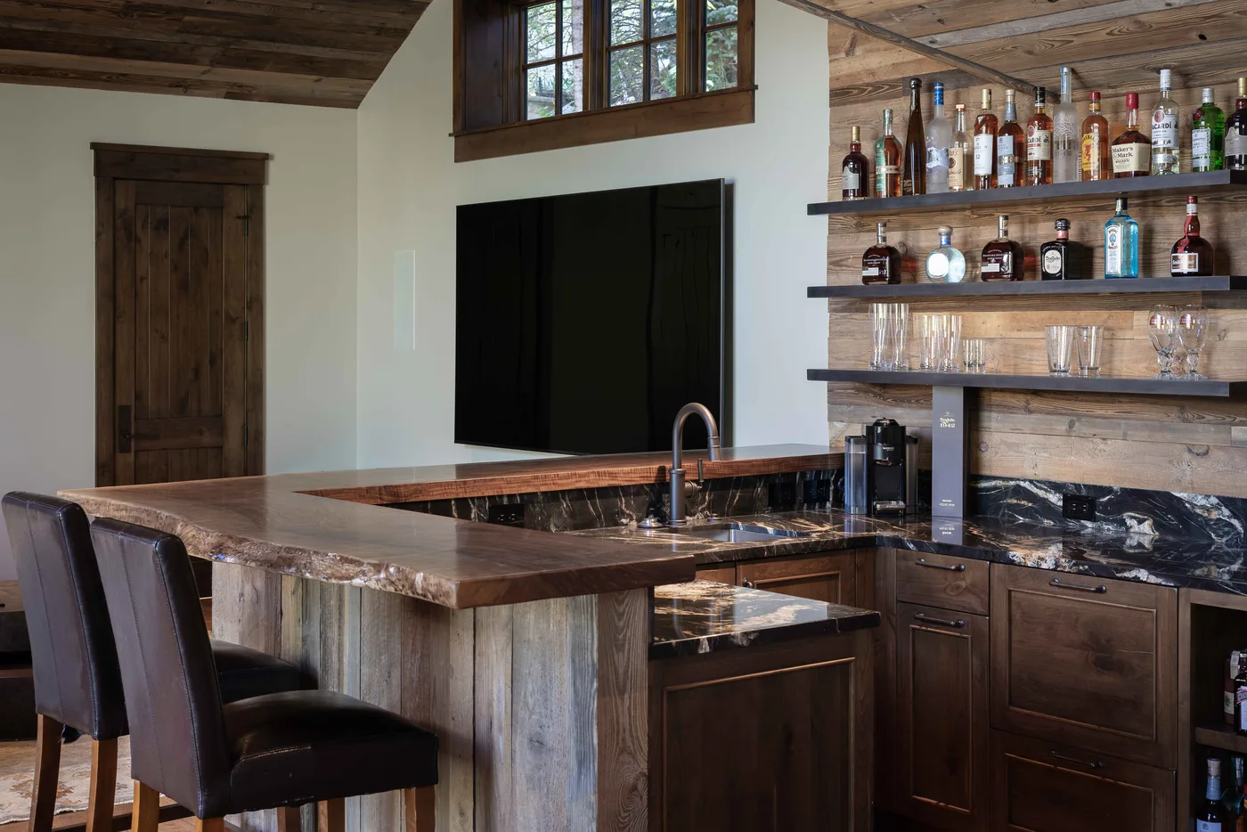 A rustic kitchen and bar with a large island, dark cabinetry, and open bottle shelves.
