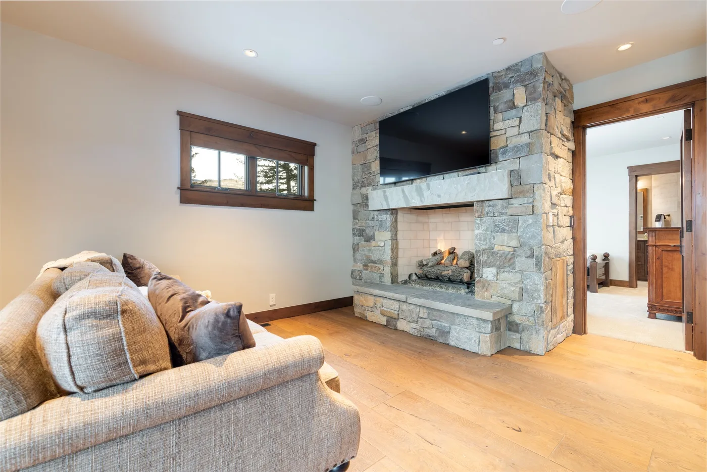 A living room with a stone fireplace, mounted television, and seating.