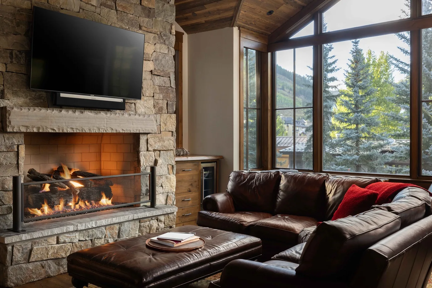 A living room with a stone fireplace, leather seating, and large windows.