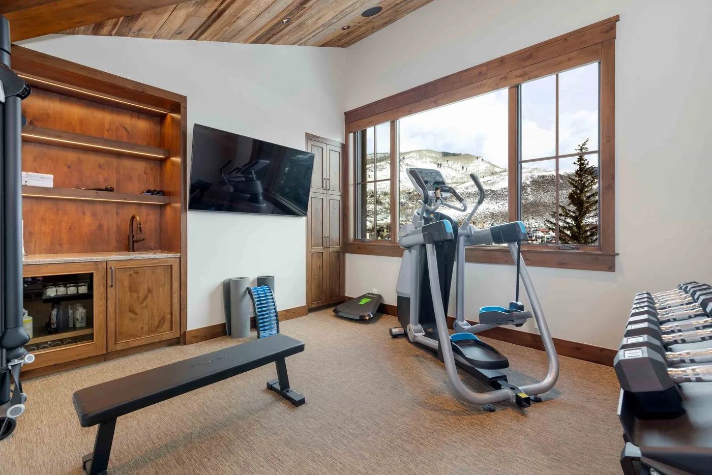 A home gym with exercise equipment and a large window overlooking a snowy landscape.