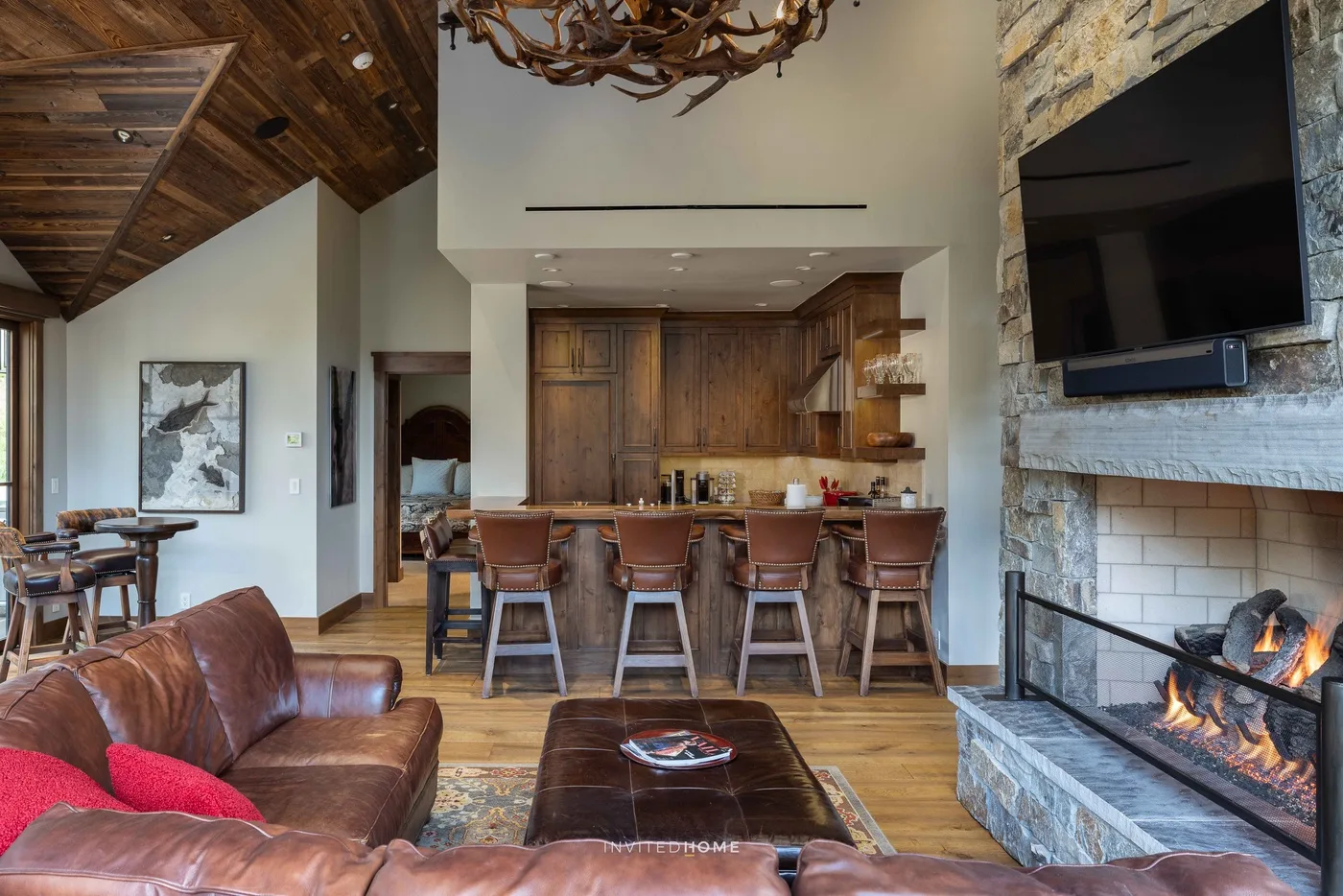 A rustic living room opens onto a kitchen and dining area, with a fireplace and leather seating.