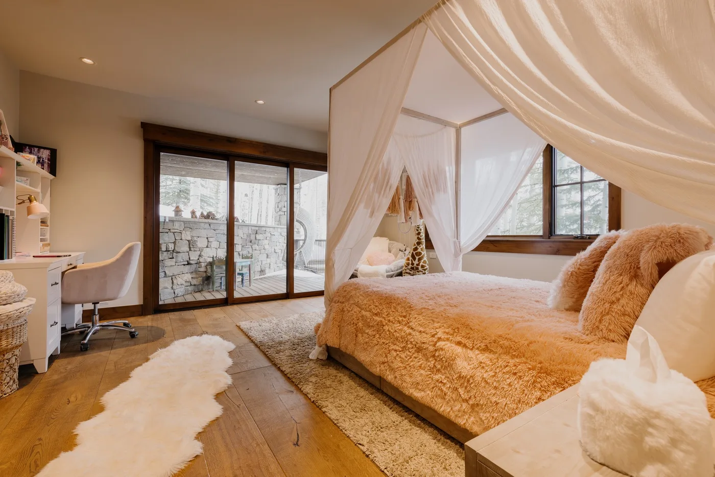 A bedroom with a canopy bed, a desk, and glass doors opening onto a patio.