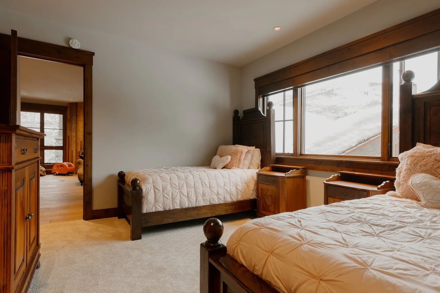 A bedroom with two beds, wooden furniture, and a large window.