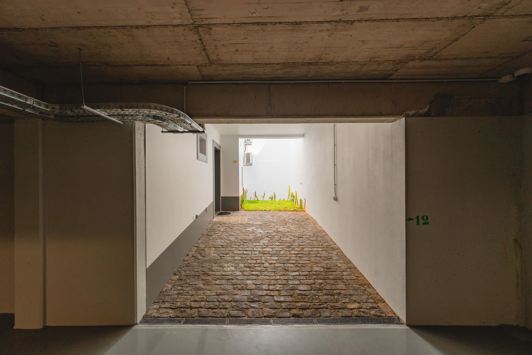 A covered passage opens onto a cobblestone ramp leading toward a bright outdoor area.