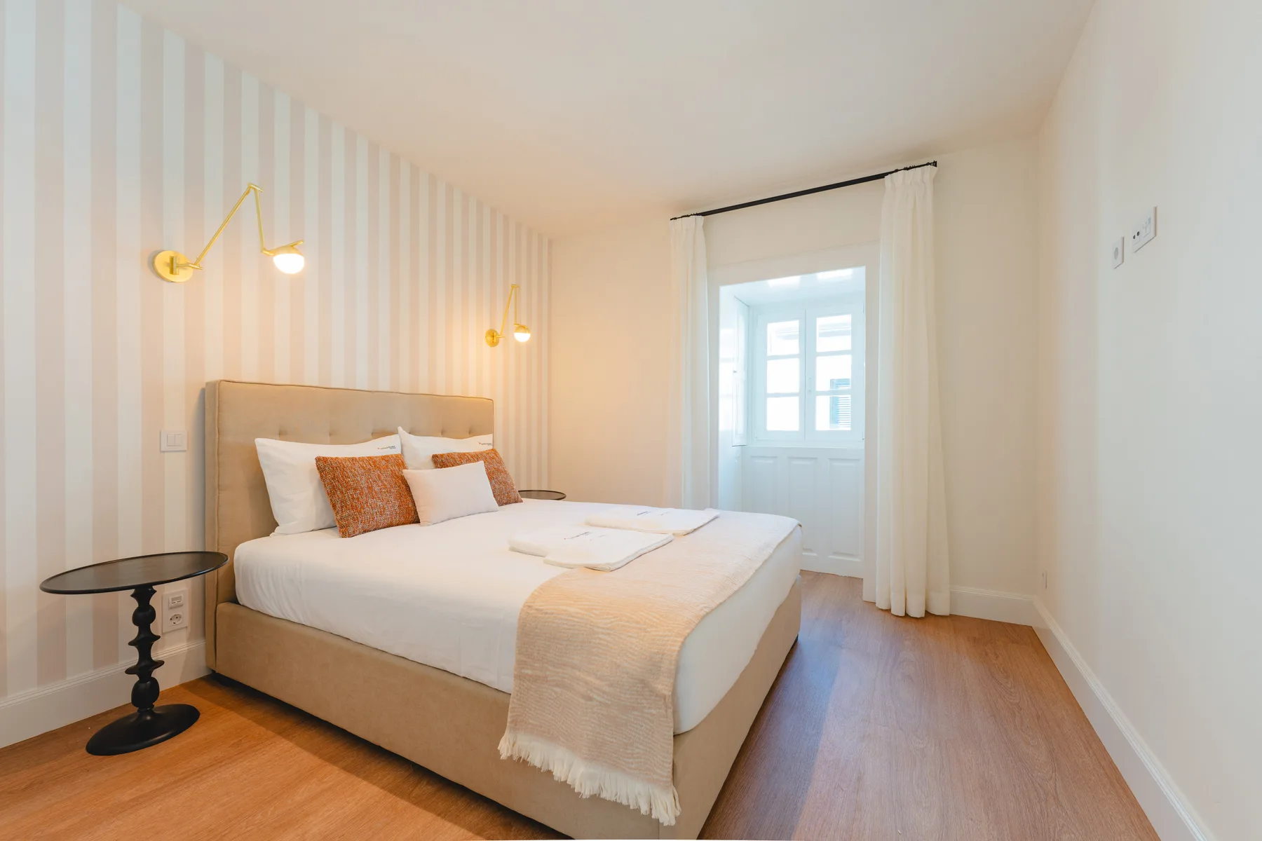 Un dormitorio con una cama, papel pintado a rayas y una ventana con cortinas.