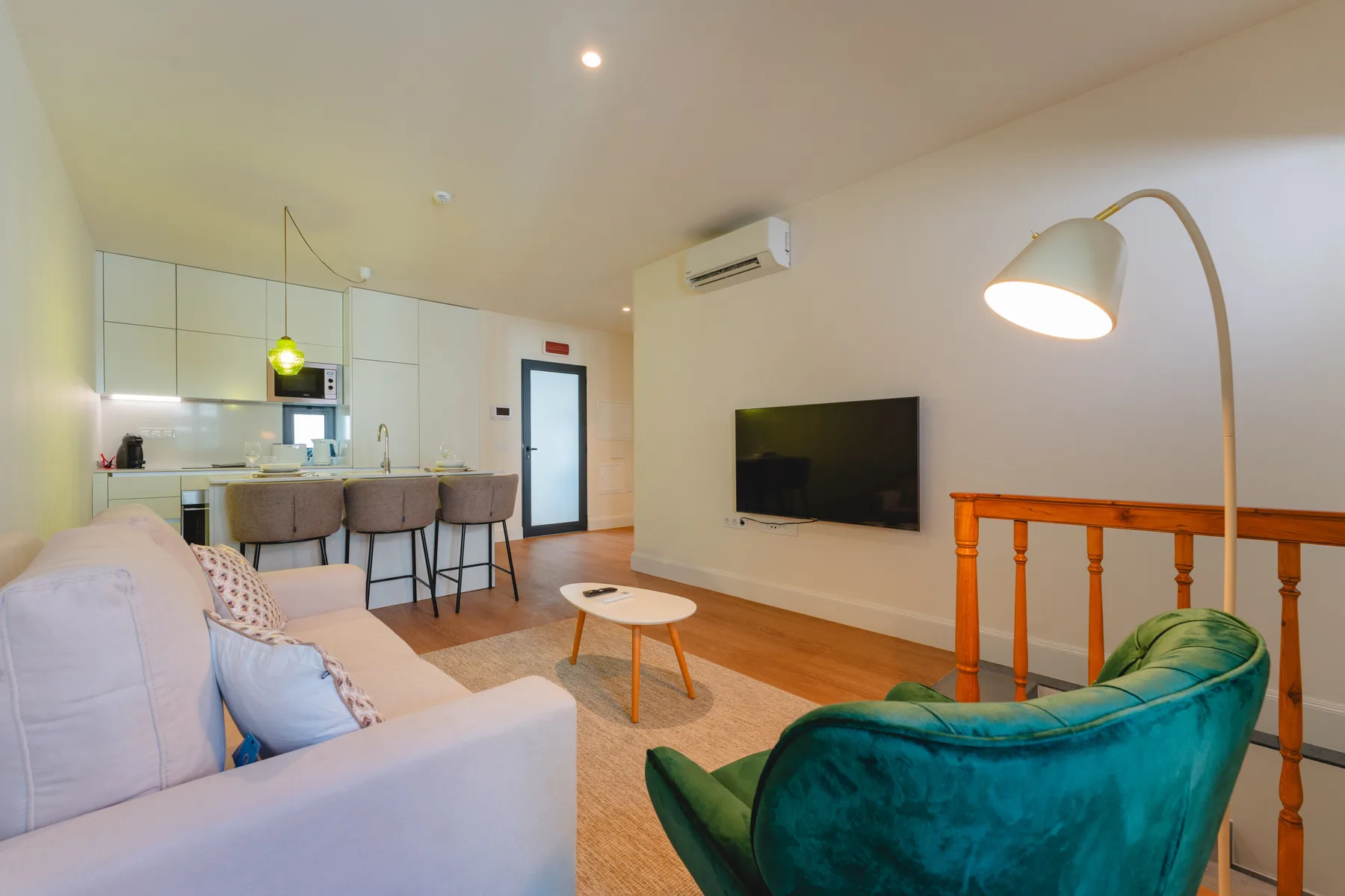 Sala de estar con asientos, un televisor montado en la pared y cocina abierta.