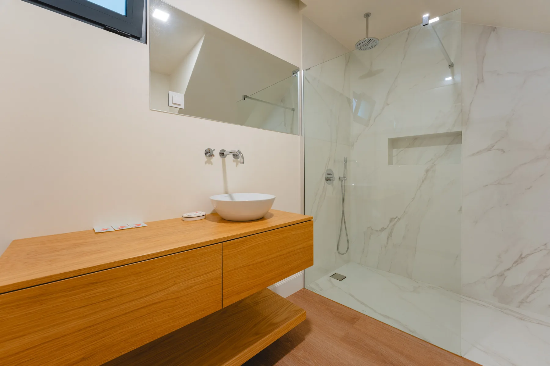 Un baño con un mueble de madera y una ducha de vidrio.