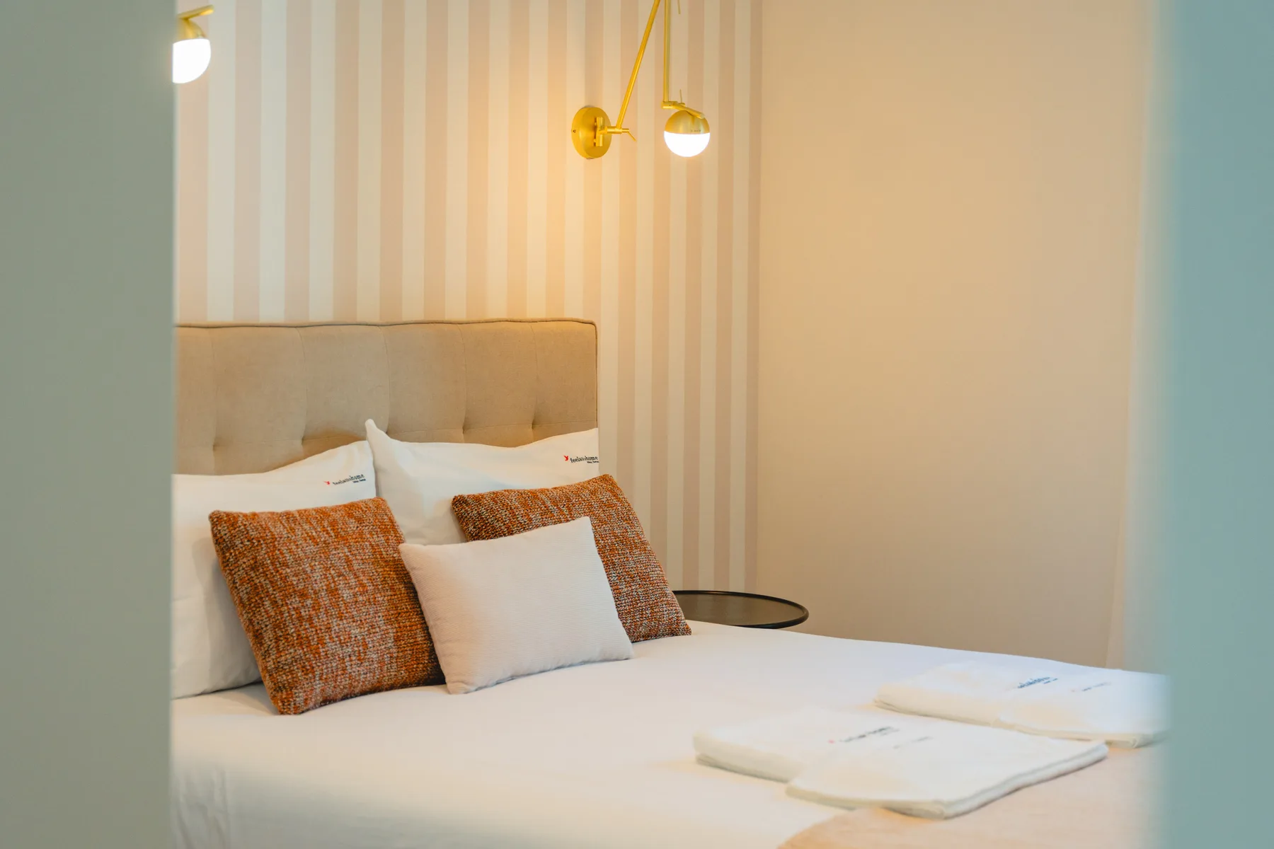 Un dormitorio con una cama bien hecha y papel pintado a rayas.