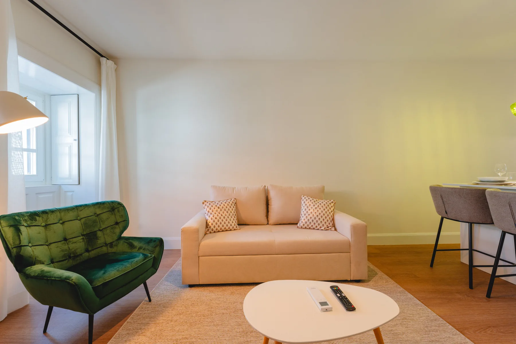 Una sala de estar con un sofá, asientos verdes y una pequeña zona de comedor.