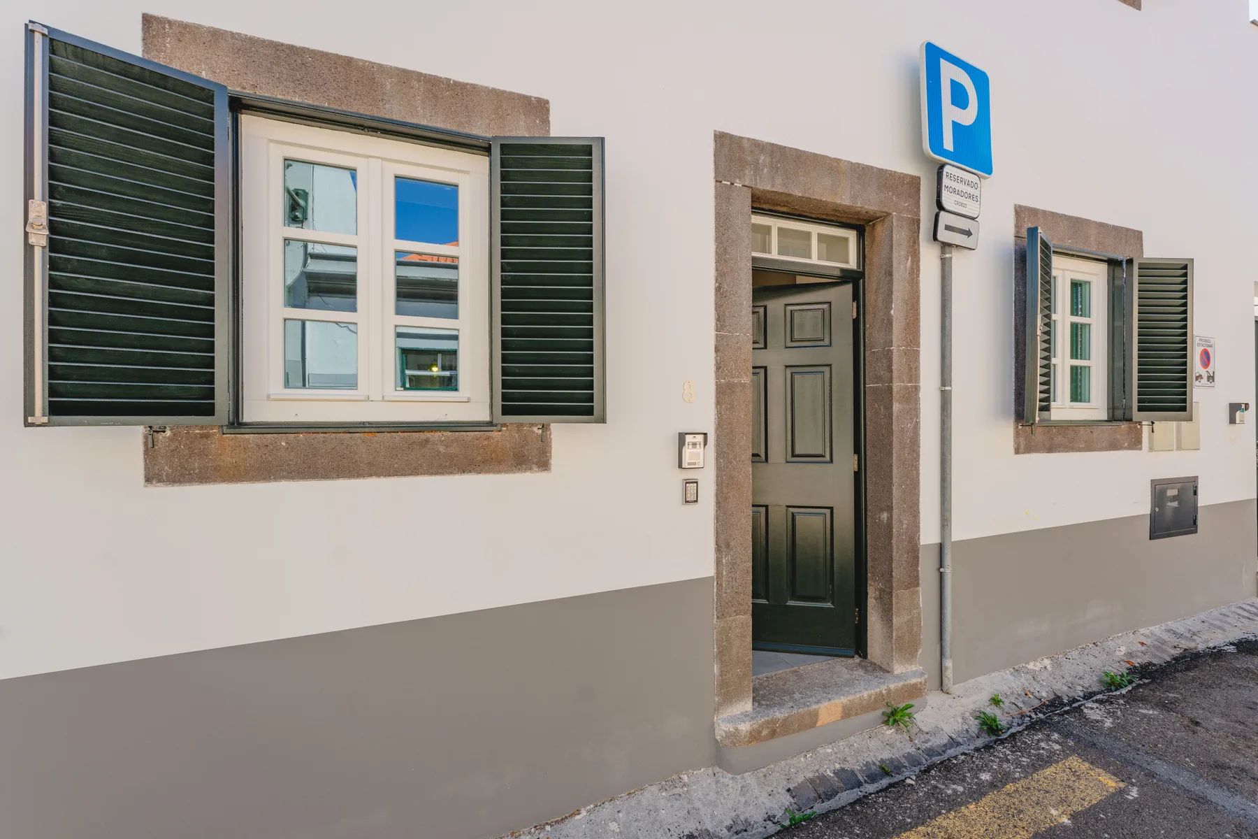 Fachada de edificio a la calle con ventanas con contraventanas y una puerta oscura.
