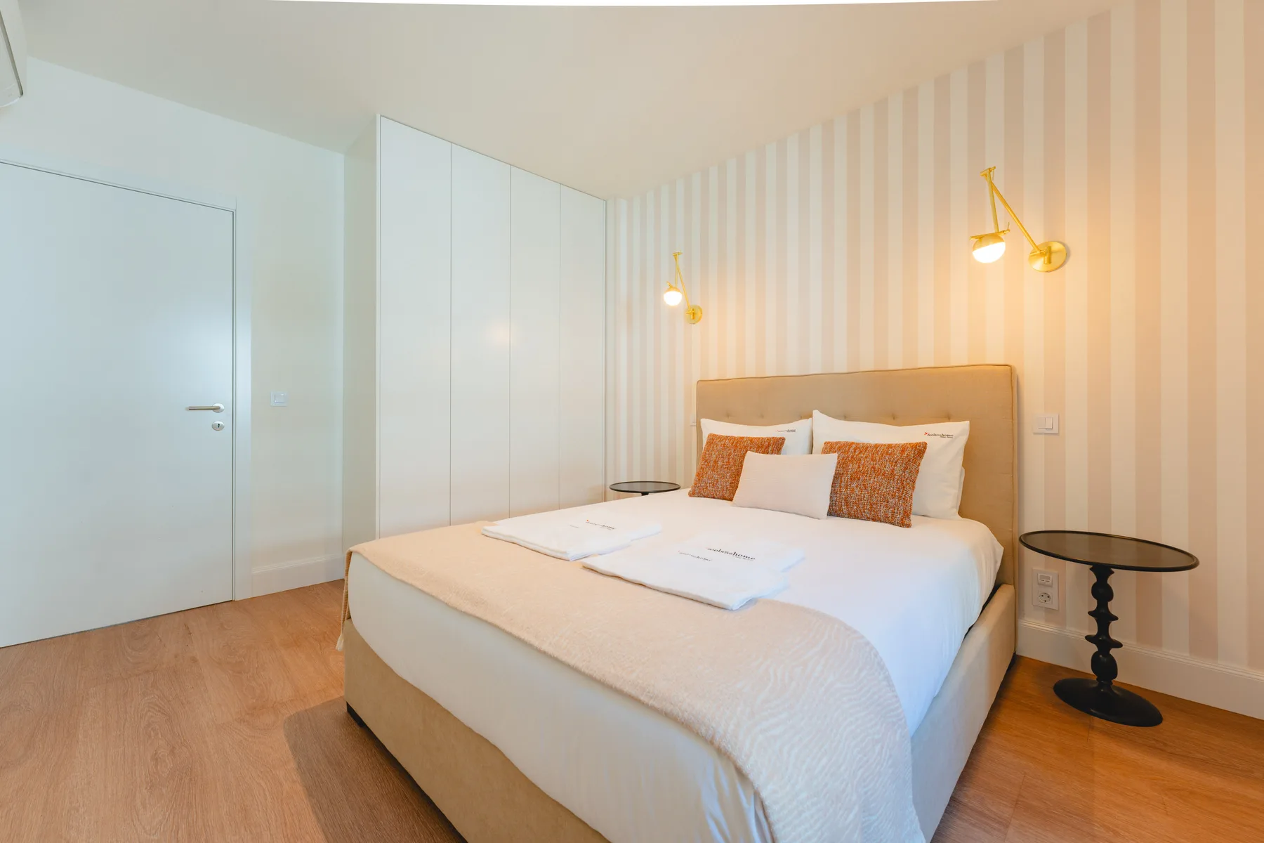 Un dormitorio con una cama bien hecha, mesillas de noche y papel pintado a rayas.