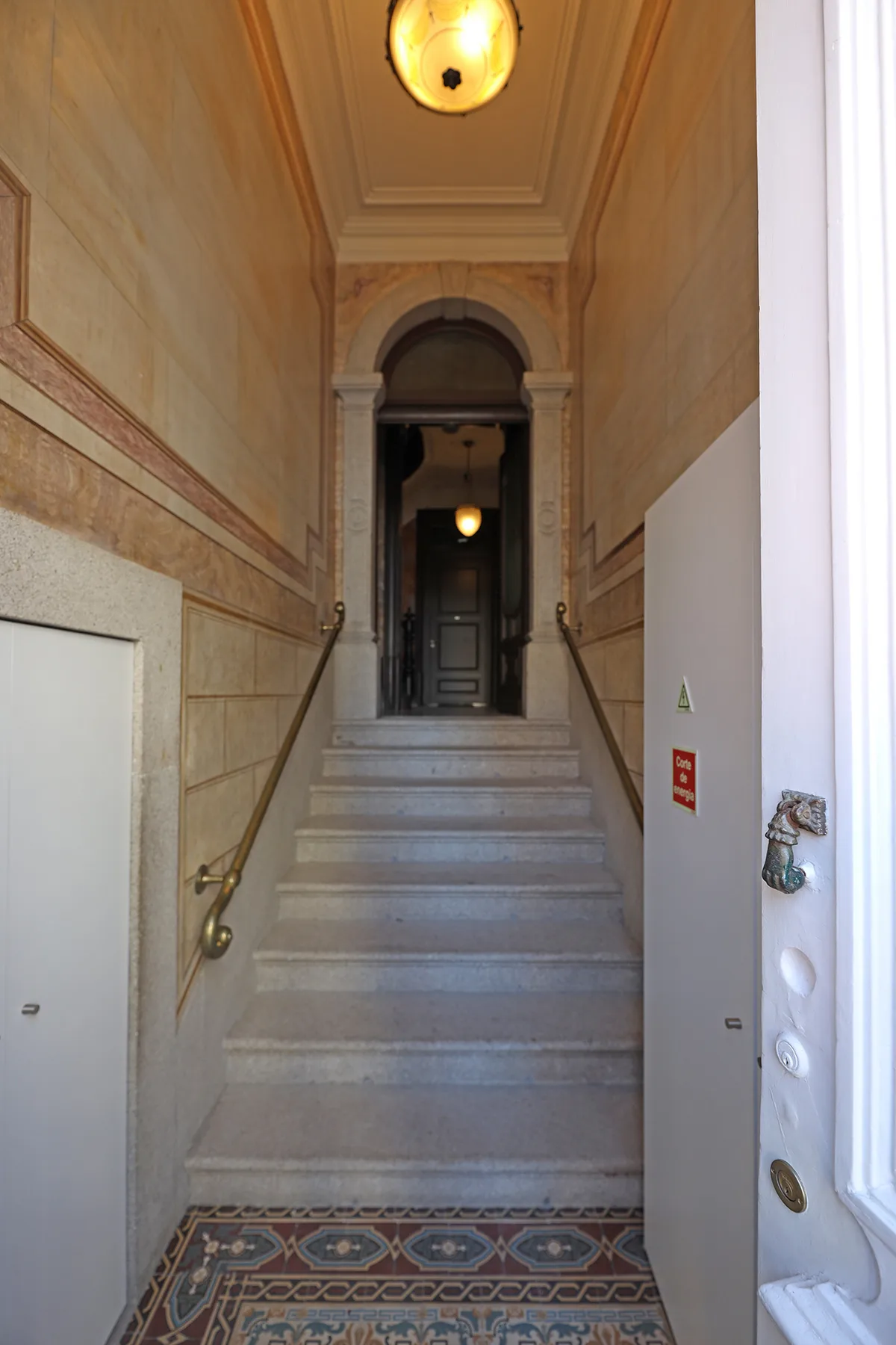 An ornate stairway rises toward a dark doorway beneath a decorative ceiling.