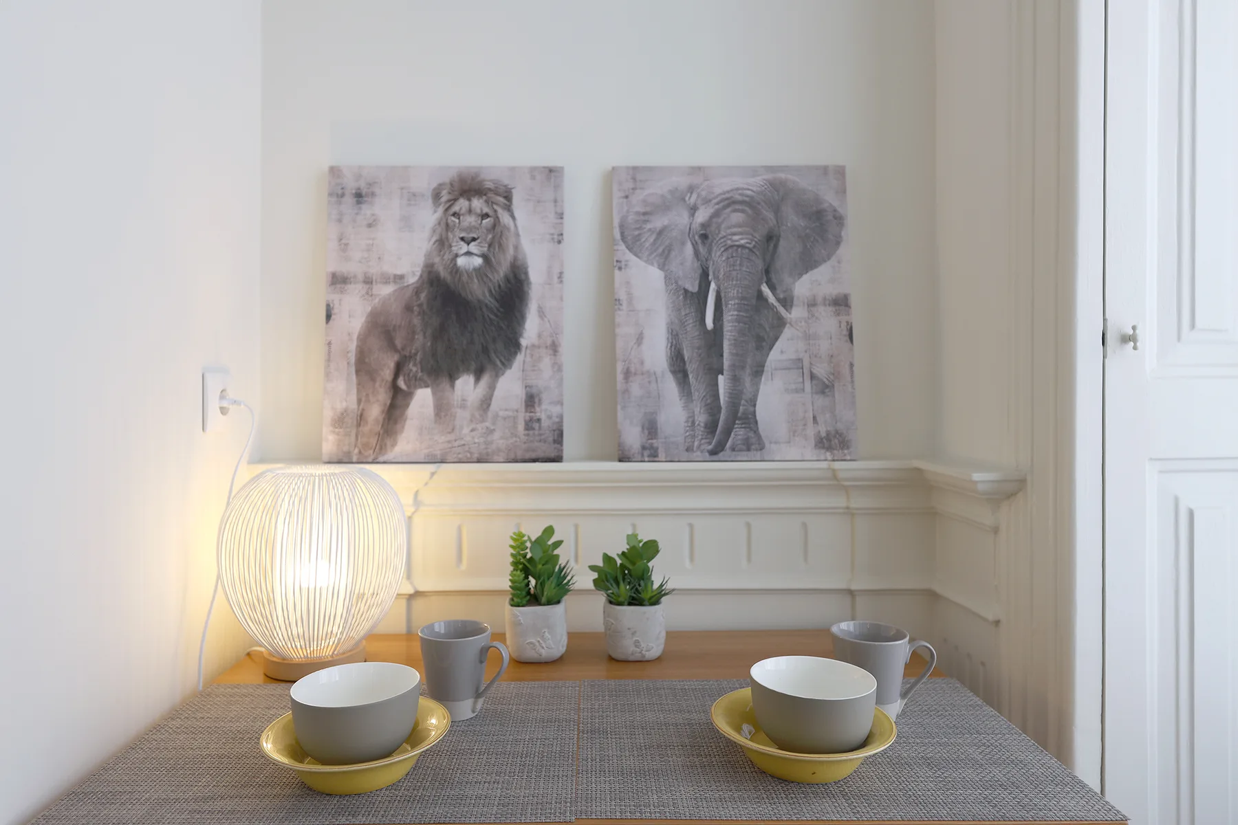 A dining table is set with bowls and cups beneath framed animal artwork.
