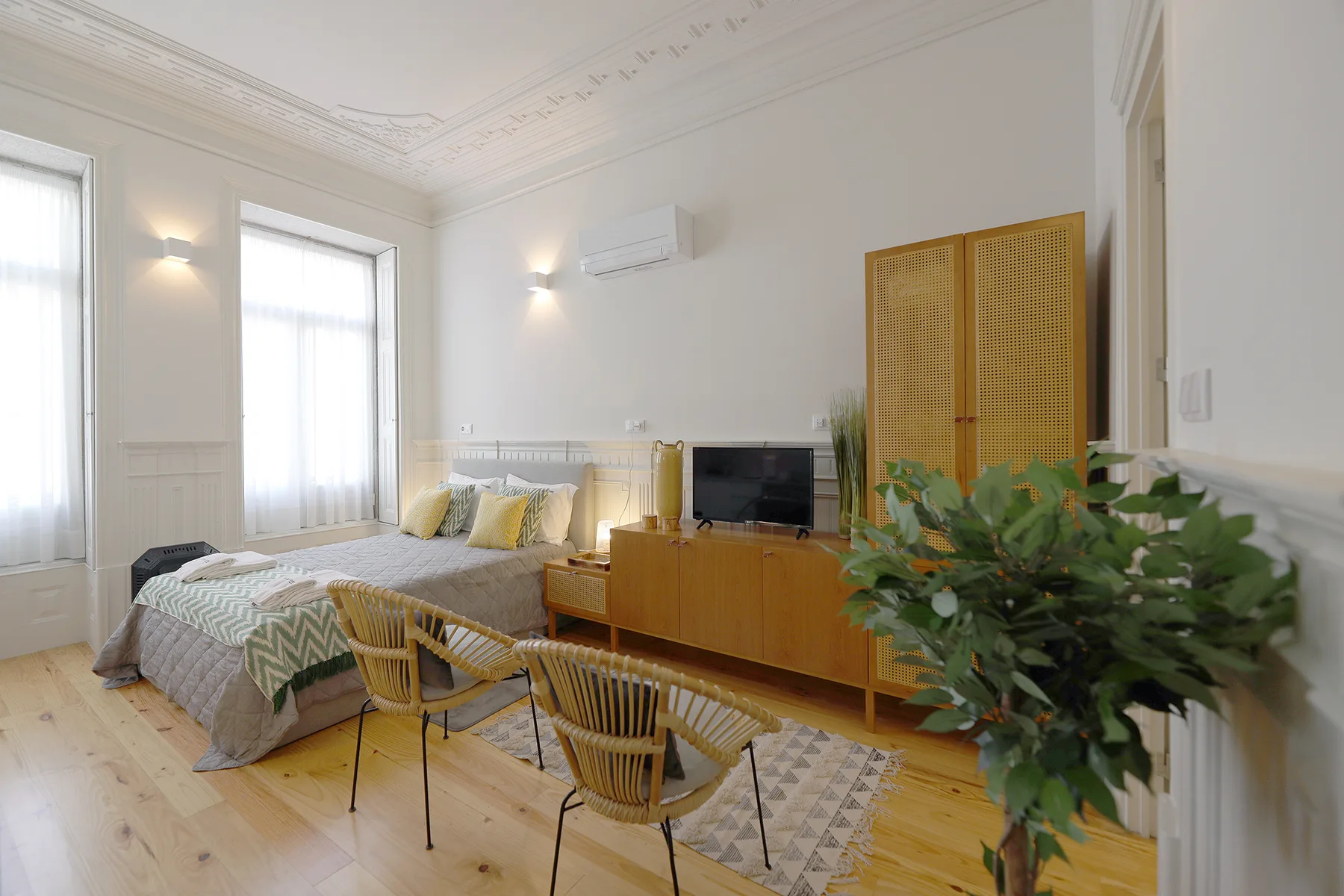 A bright bedroom with a bed, television, and woven seating.