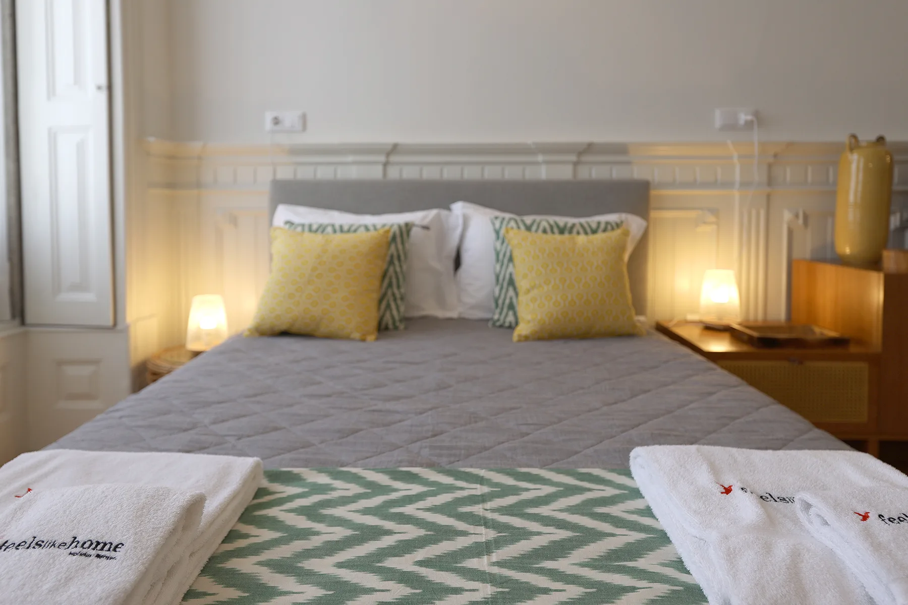 A bedroom with a neatly made bed, patterned pillows, and bedside lamps.