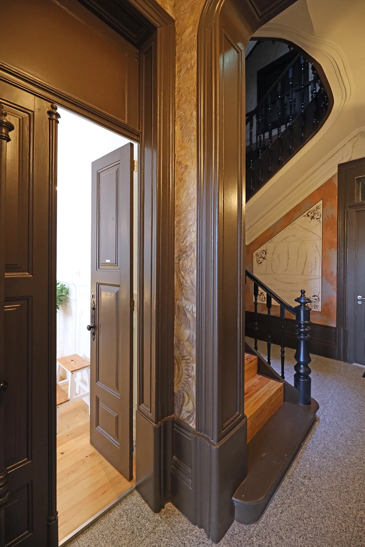 An ornate hallway opens onto a bright room, with a staircase beside it.