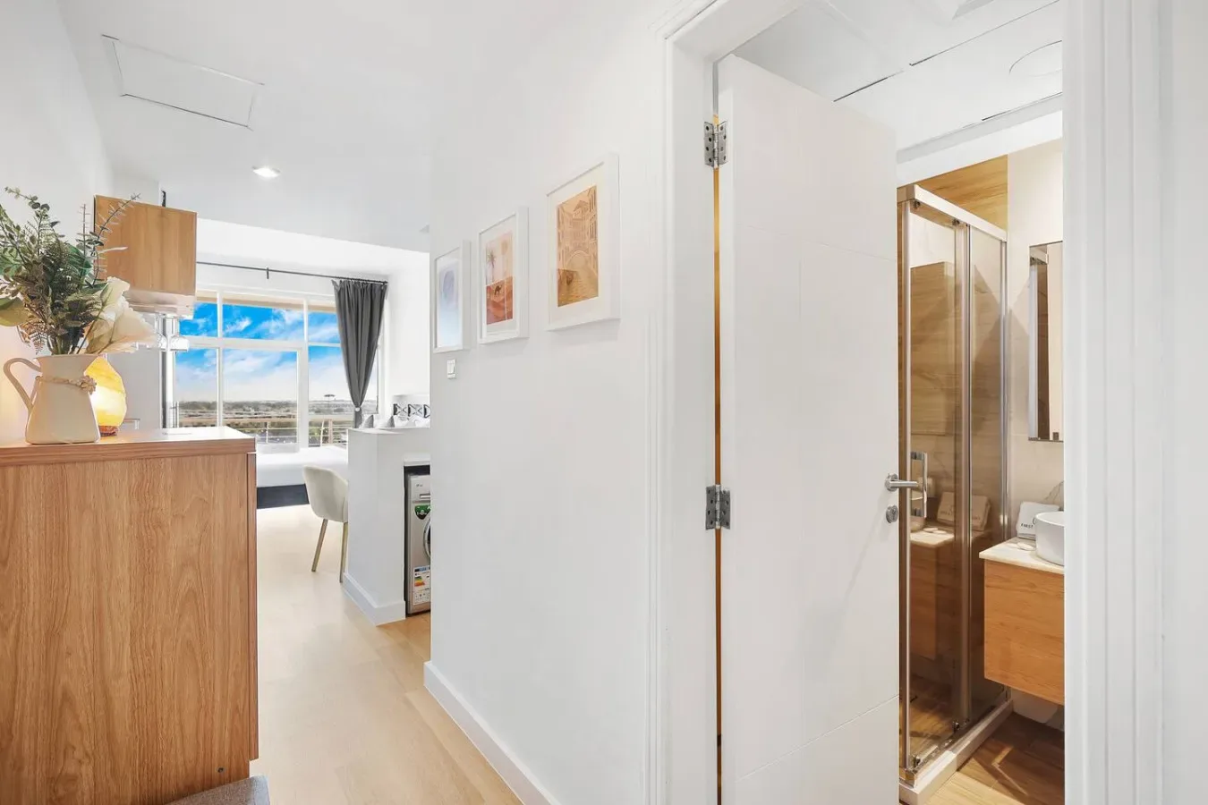 A bright apartment interior with a kitchenette, dining area, and bathroom doorway.
