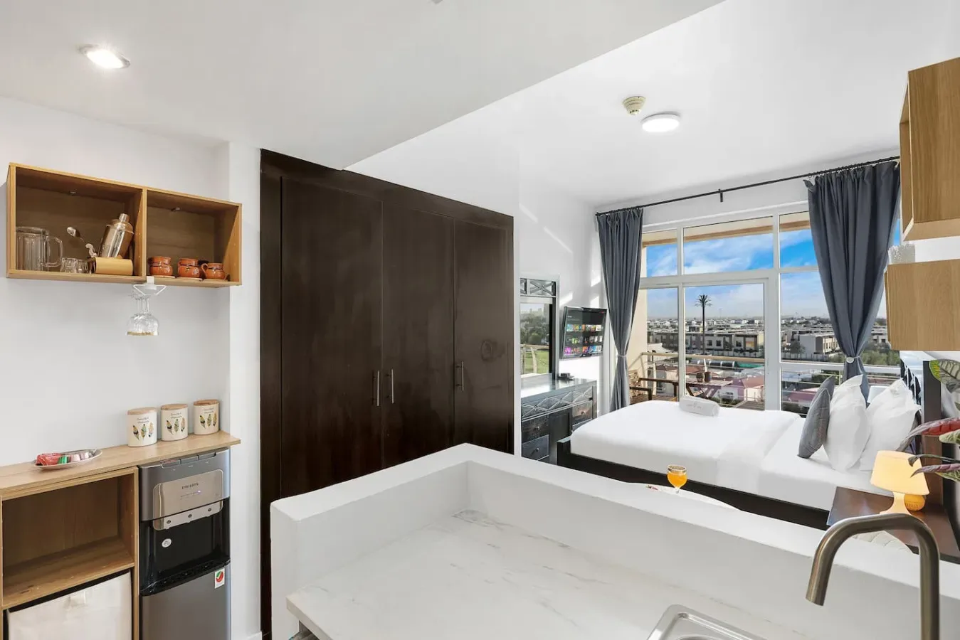 A bedroom with a bed beside large windows overlooking the city.