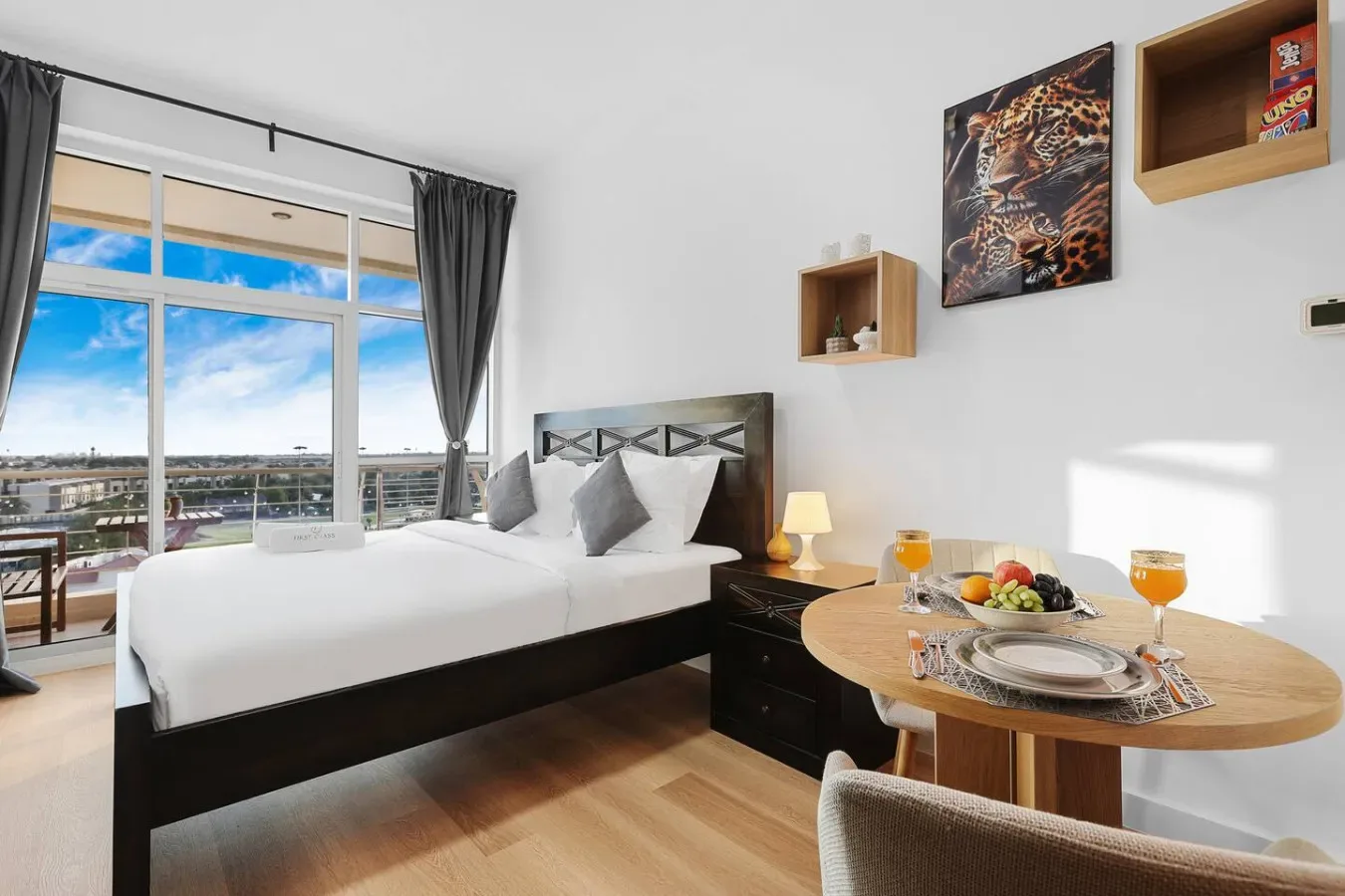 A bright bedroom with a bed beside floor-to-ceiling windows and a small dining table.