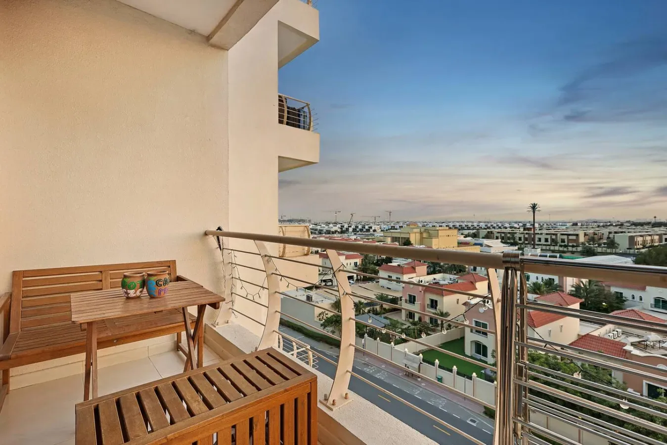 A balcony with wooden seating overlooks a residential neighborhood at sunset.