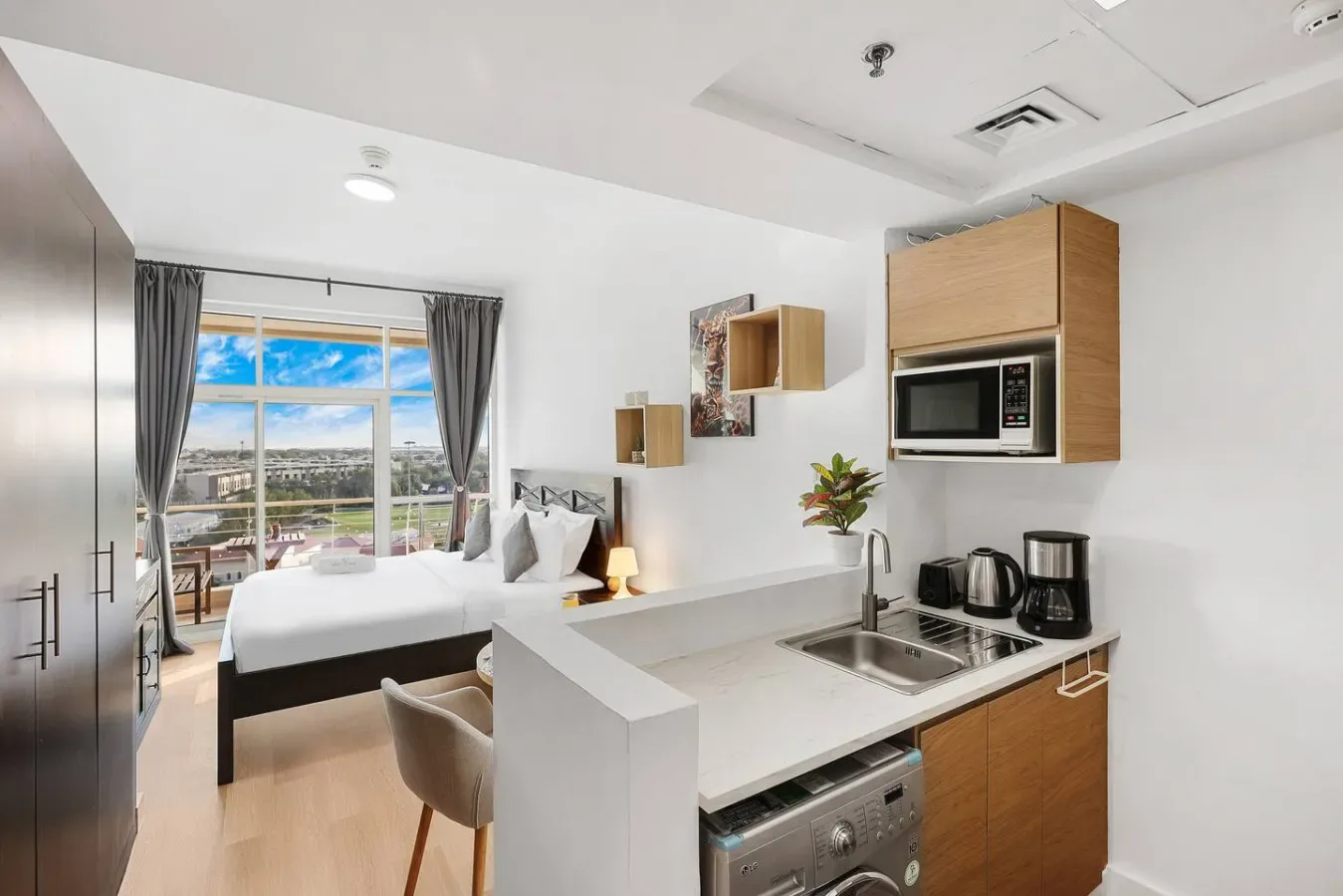 A studio room with a bed beside a compact kitchen and a large window.