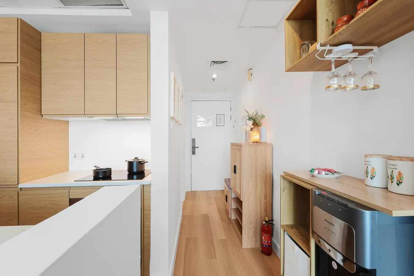 A compact kitchen with light wood cabinets, a counter, and a hallway beyond.