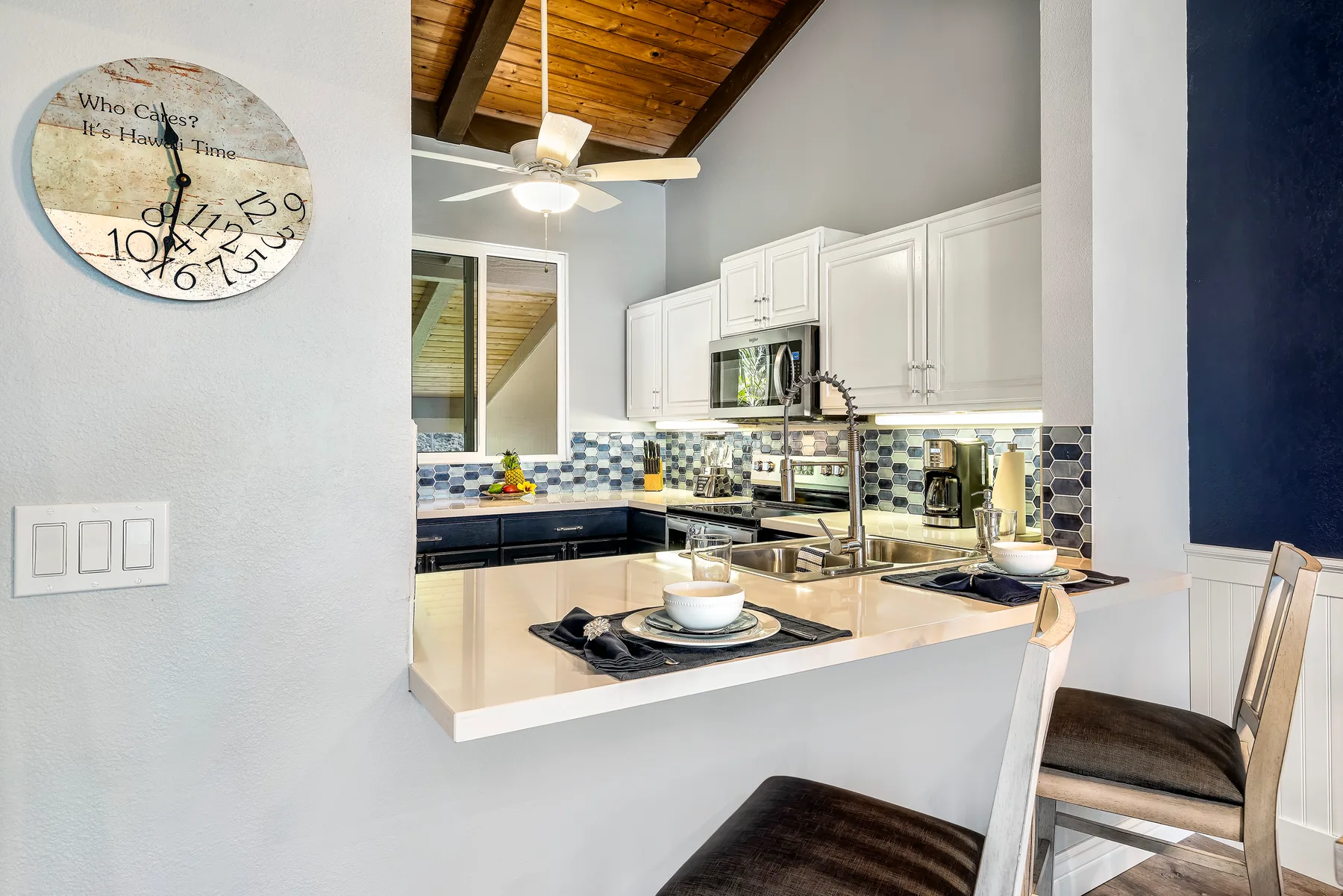 A bright kitchen with a breakfast bar, white cabinets, and a wood ceiling.