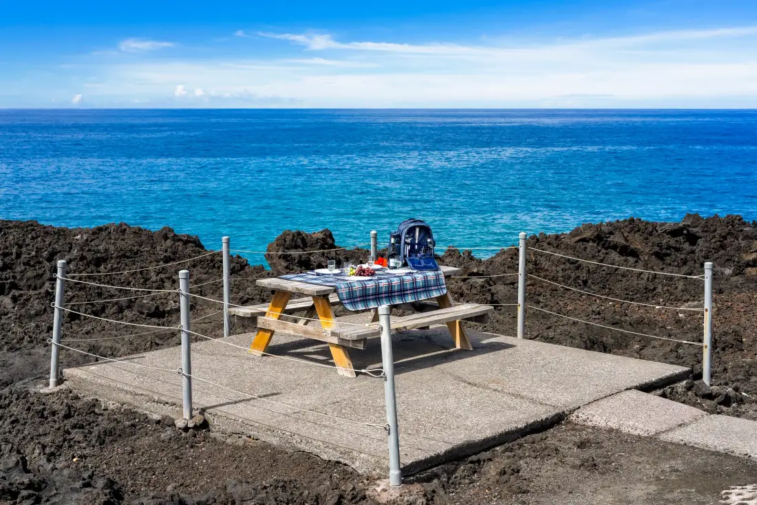 A picnic table sits on a paved seaside lookout overlooking the blue ocean.