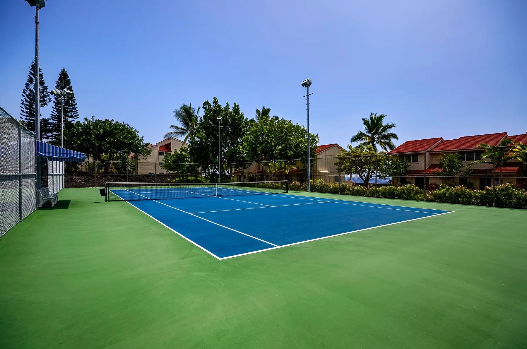 An outdoor tennis court with a blue playing surface and green surroundings.