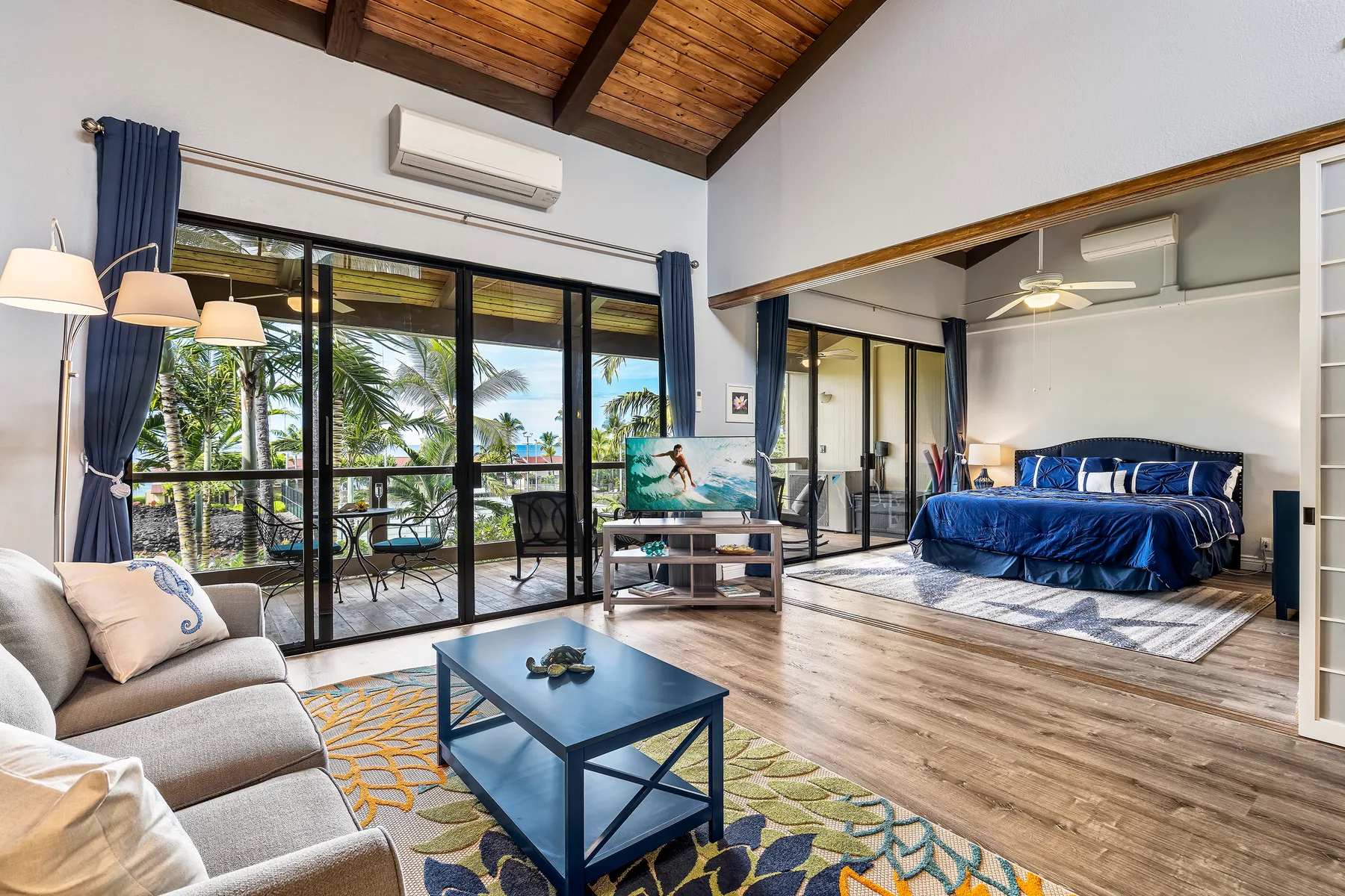A bright bedroom and sitting area open onto a balcony with tropical views.