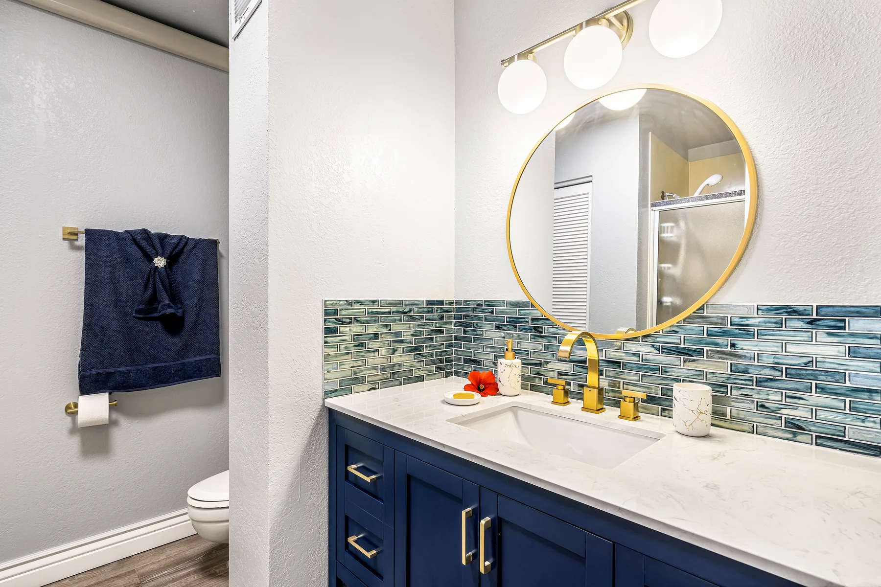 A bathroom vanity with a round mirror, blue cabinets, and tiled backsplash.