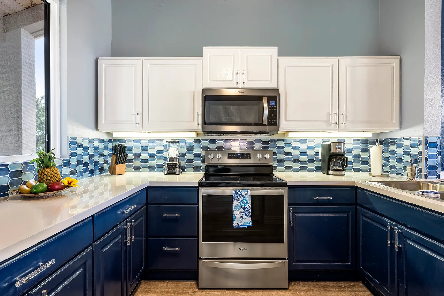 A kitchen with dark blue lower cabinets, white upper cabinets, and a stainless steel range.