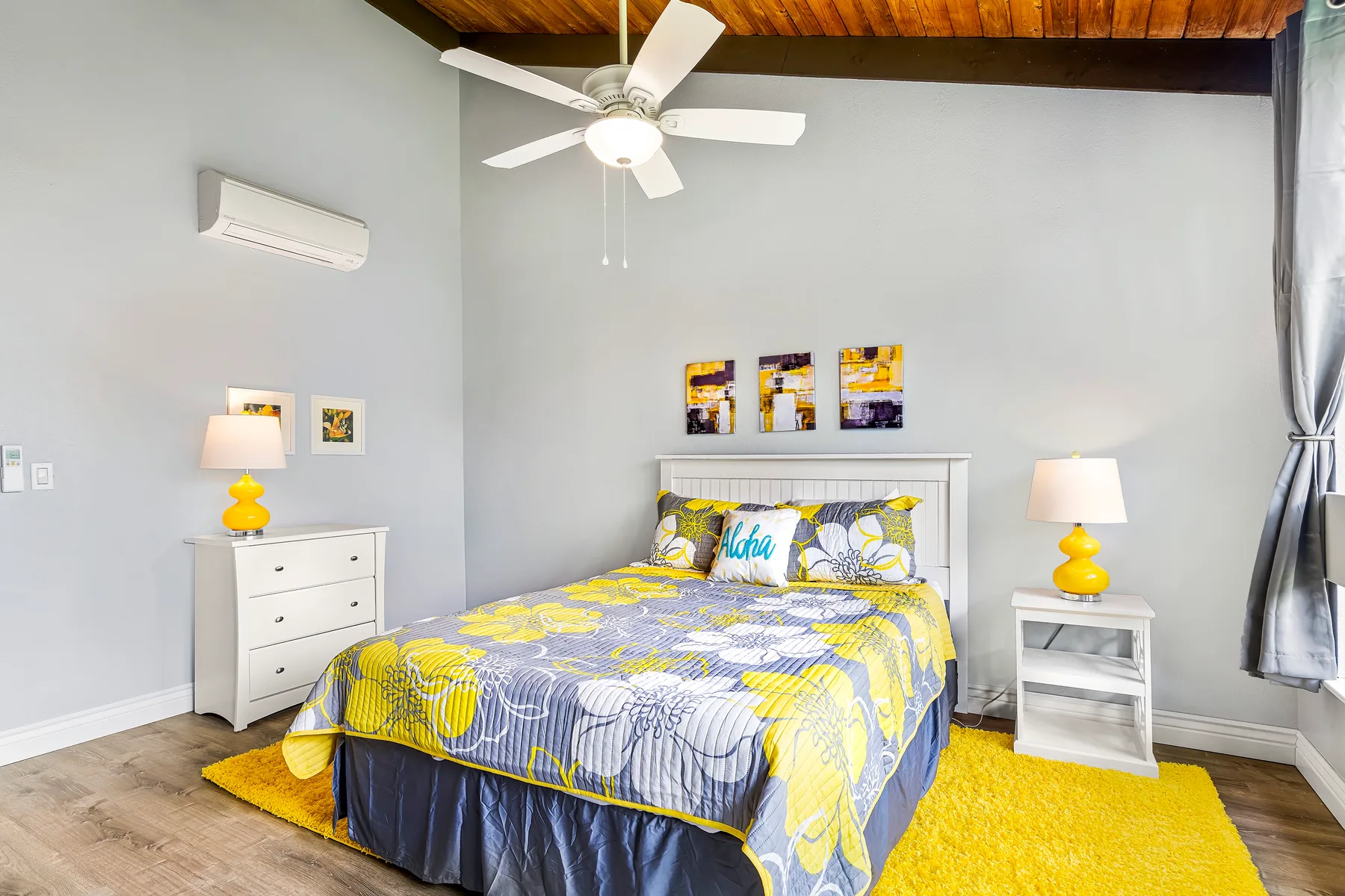 A bedroom with a bed covered in yellow and gray bedding beneath a ceiling fan.