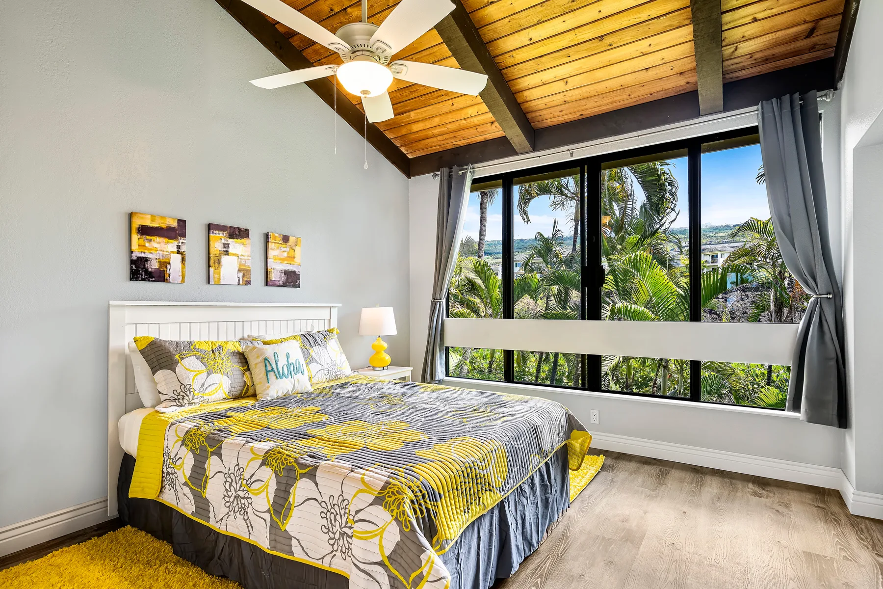 A bedroom with a bed beneath large windows overlooking greenery.
