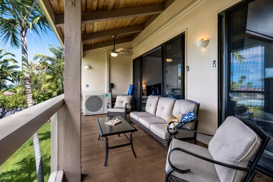 A covered outdoor seating area with cushioned chairs and a view of palm trees.