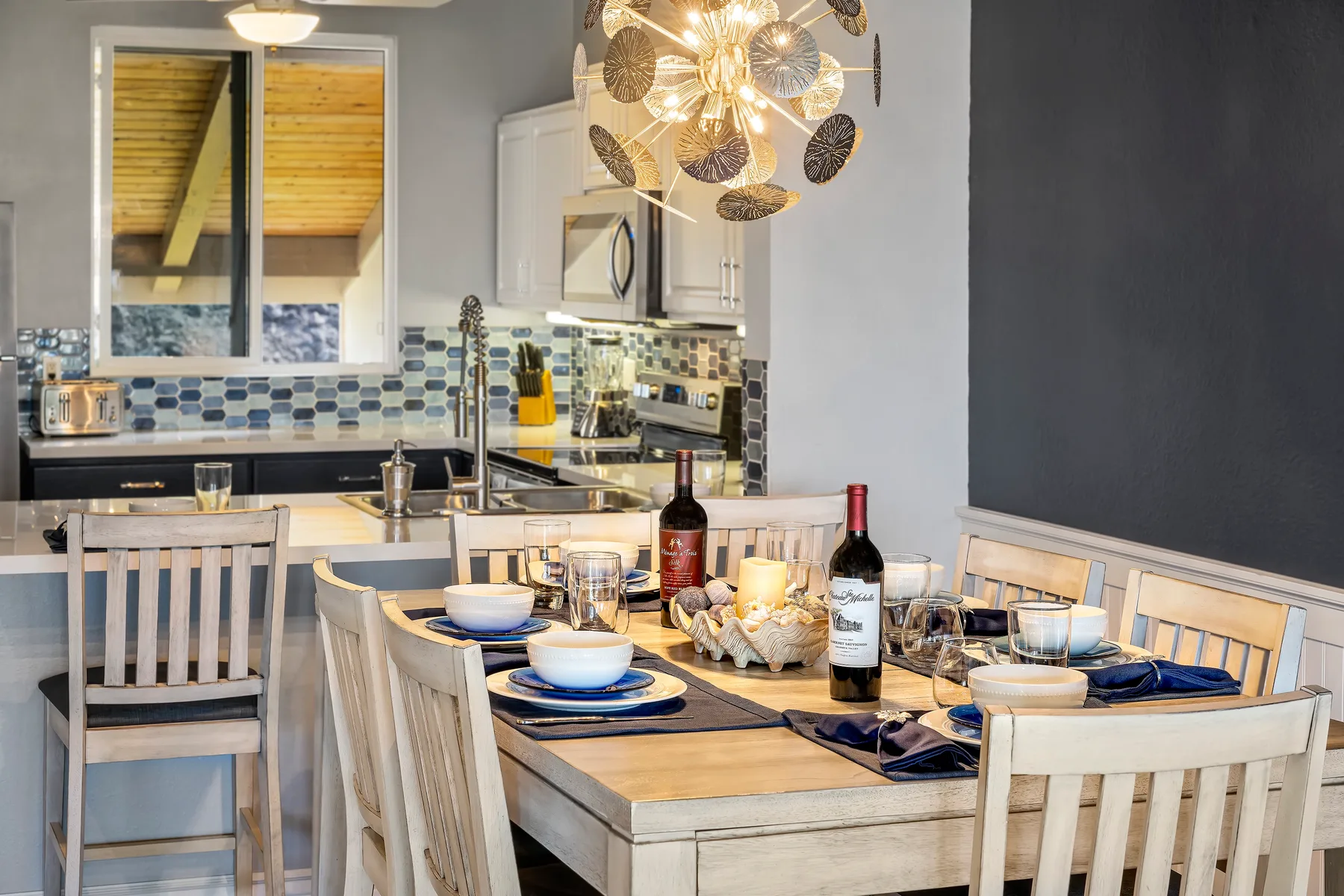 A dining table set for a meal sits beside a modern kitchen.
