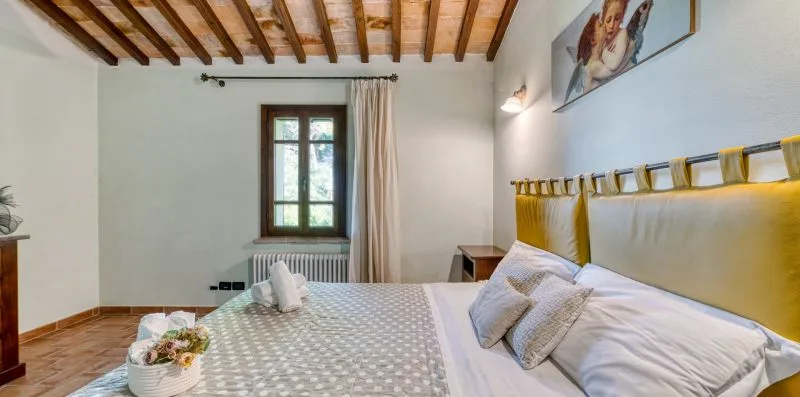A bedroom with a bed, window, and exposed wooden ceiling beams.