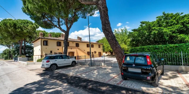 A tan building beside a paved parking area with parked vehicles and trees.