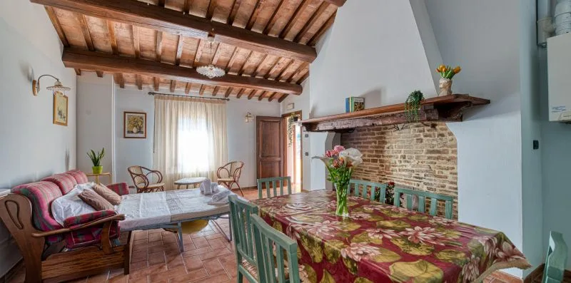 A dining room with a long table, colorful floral tablecloth, and exposed timber ceiling.