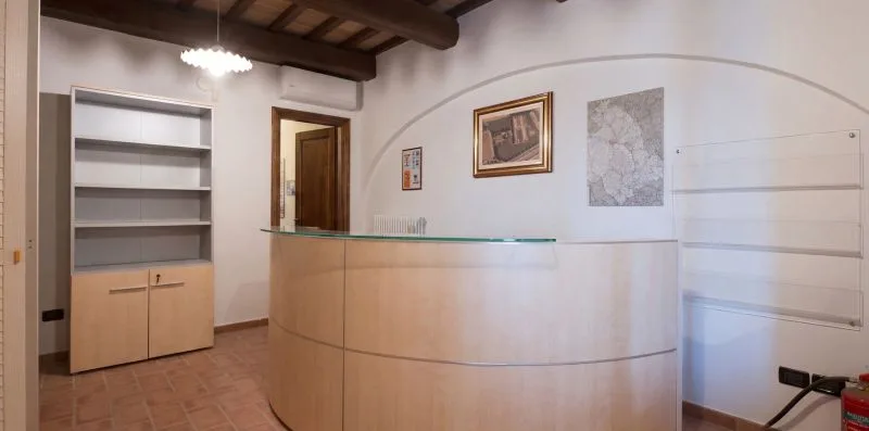 A curved reception desk stands in a room with built-in shelving and exposed ceiling beams.