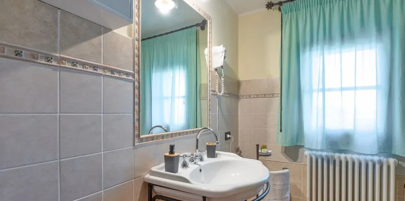 A tiled bathroom with a sink, mirror, and turquoise curtains.